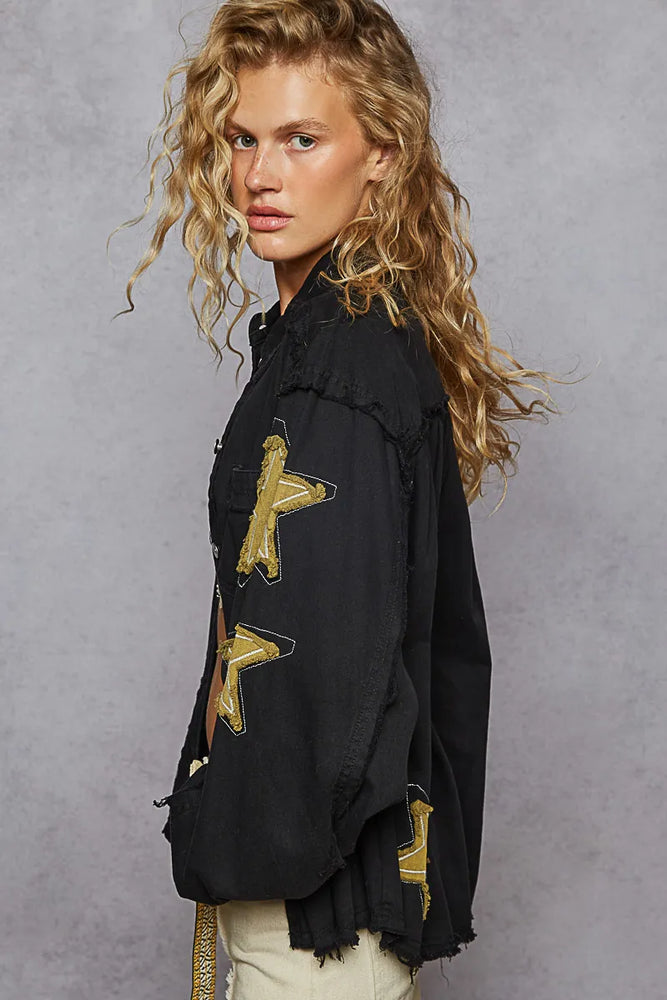 Oversized black denim jacket with gold star embroidery patches, raw distressed hem, classic collar, and chest pockets—styled for bold, modern streetwear.

