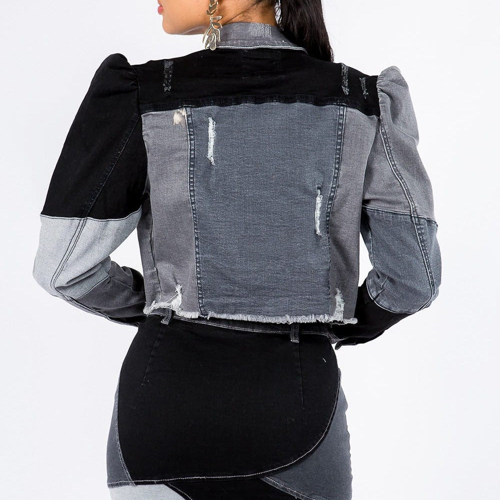 back view of the Unique Kulture American Bazi Button Up Cropped Patchwork Denim Jacket, featuring a stylish cropped length, distinctive patchwork design, frayed edge hem, and puff shoulder trims. The jacket showcases a button front closure, perfect for adding a trendy and eye-catching element to any outfit.
