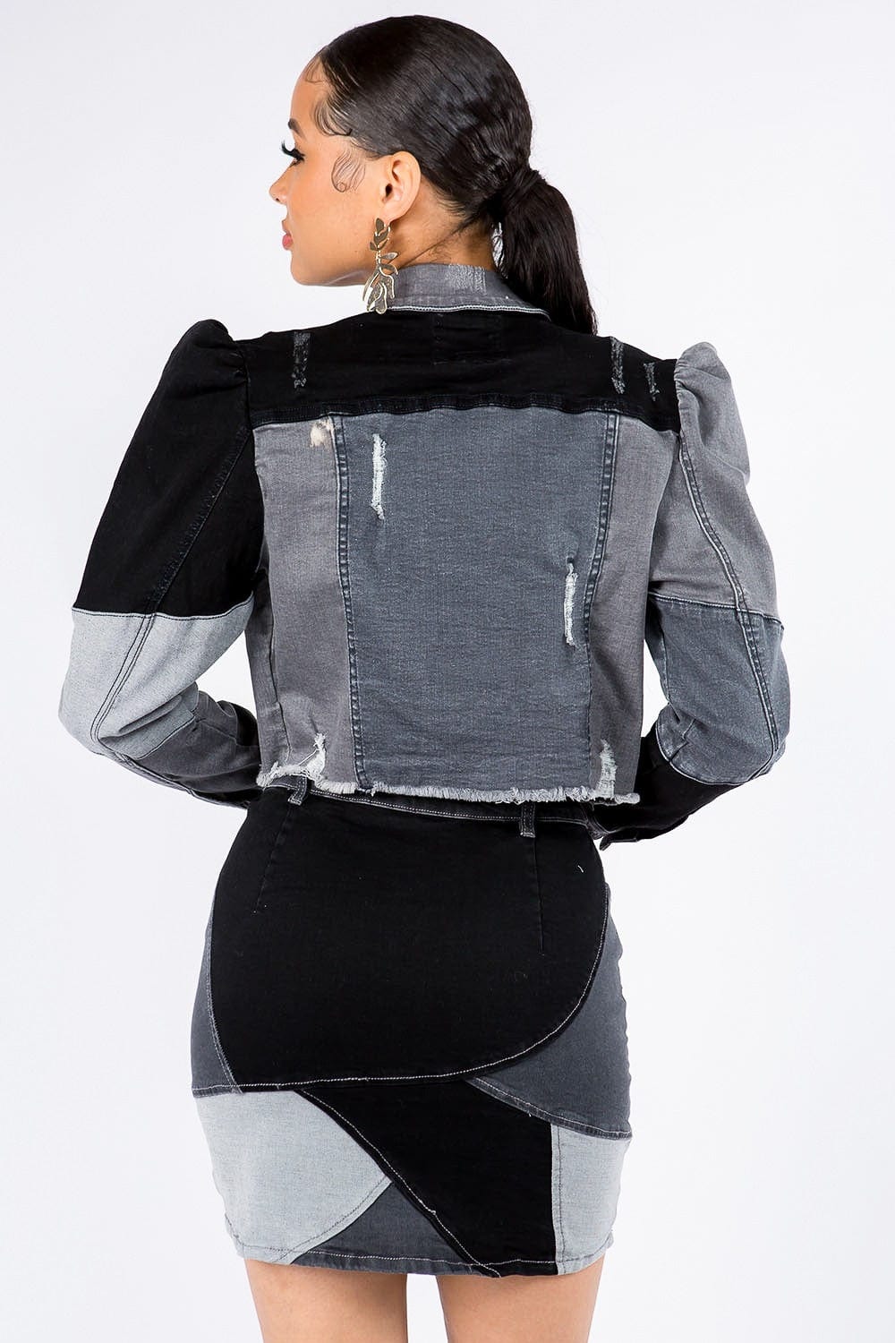 back view of the Unique Kulture American Bazi Button Up Cropped Patchwork Denim Jacket, featuring a stylish cropped length, distinctive patchwork design, frayed edge hem, and puff shoulder trims. The jacket showcases a button front closure, perfect for adding a trendy and eye-catching element to any outfit.
