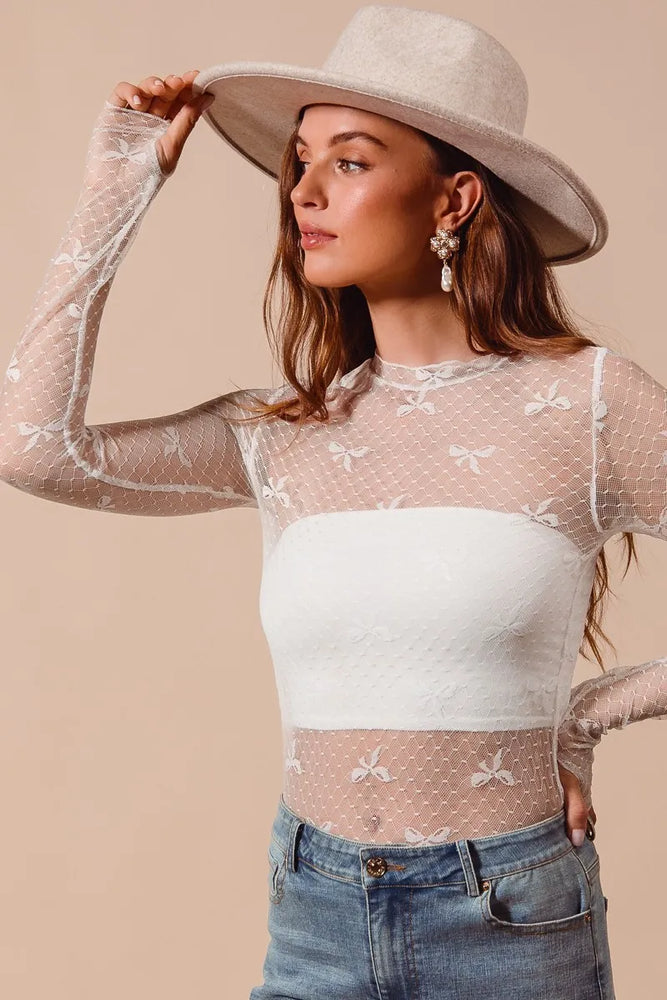 Sheer mesh lace top with bow ribbon pattern and floral embroidery, long sleeves, fitted silhouette, and crew neckline—styled for romantic and elegant layering.

