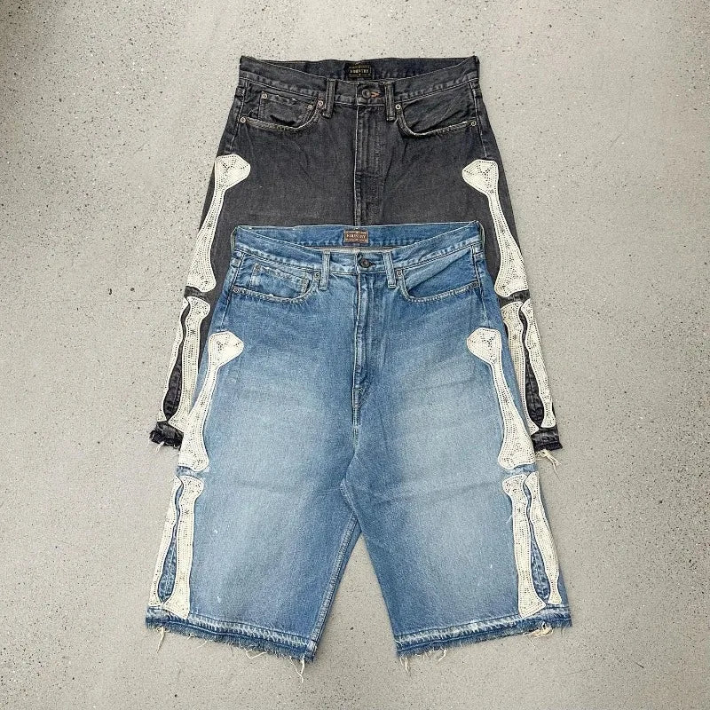 Blue denim shorts with white skeleton bone patches on each side and raw frayed hems, laid flat on a concrete background.


