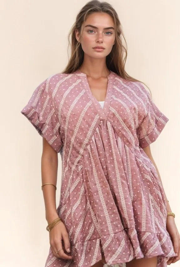 Model wearing an embroidered V-neck ruffled mini dress from Unique Kulture, featuring flutter sleeves and a tiered boho silhouette in dusty pink.

