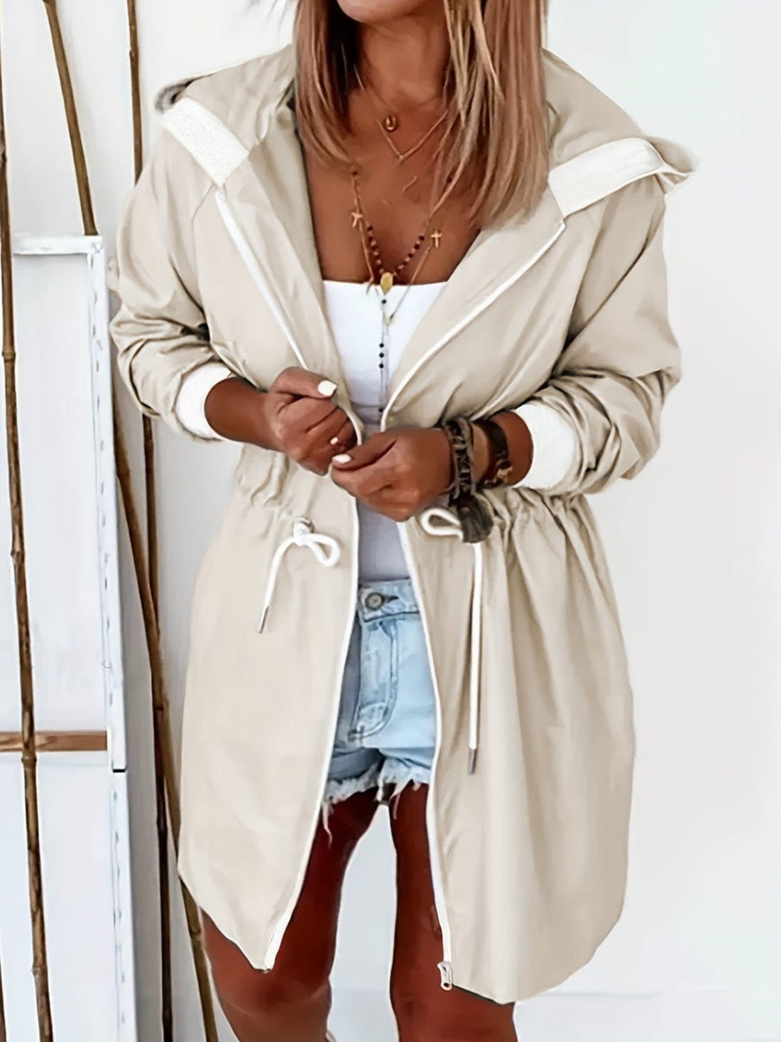 A fashionable Unique Kulture Drawstring Long Sleeve Hooded Trench Coat featuring a drawstring waist and a stylish hood. The coat is displayed against a neutral background, showcasing its lightweight design and functional pockets. Made from a blend of 95% polyester and 5% elastane, this versatile trench coat is perfect for layering and adds a chic touch to any outfit