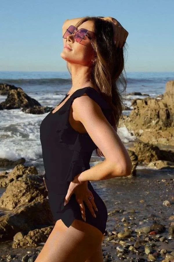 Model wearing a solid one-shoulder ruffle one-piece swimsuit from Unique Kulture, featuring a chic ruffle detail and flattering silhouette. Side View
