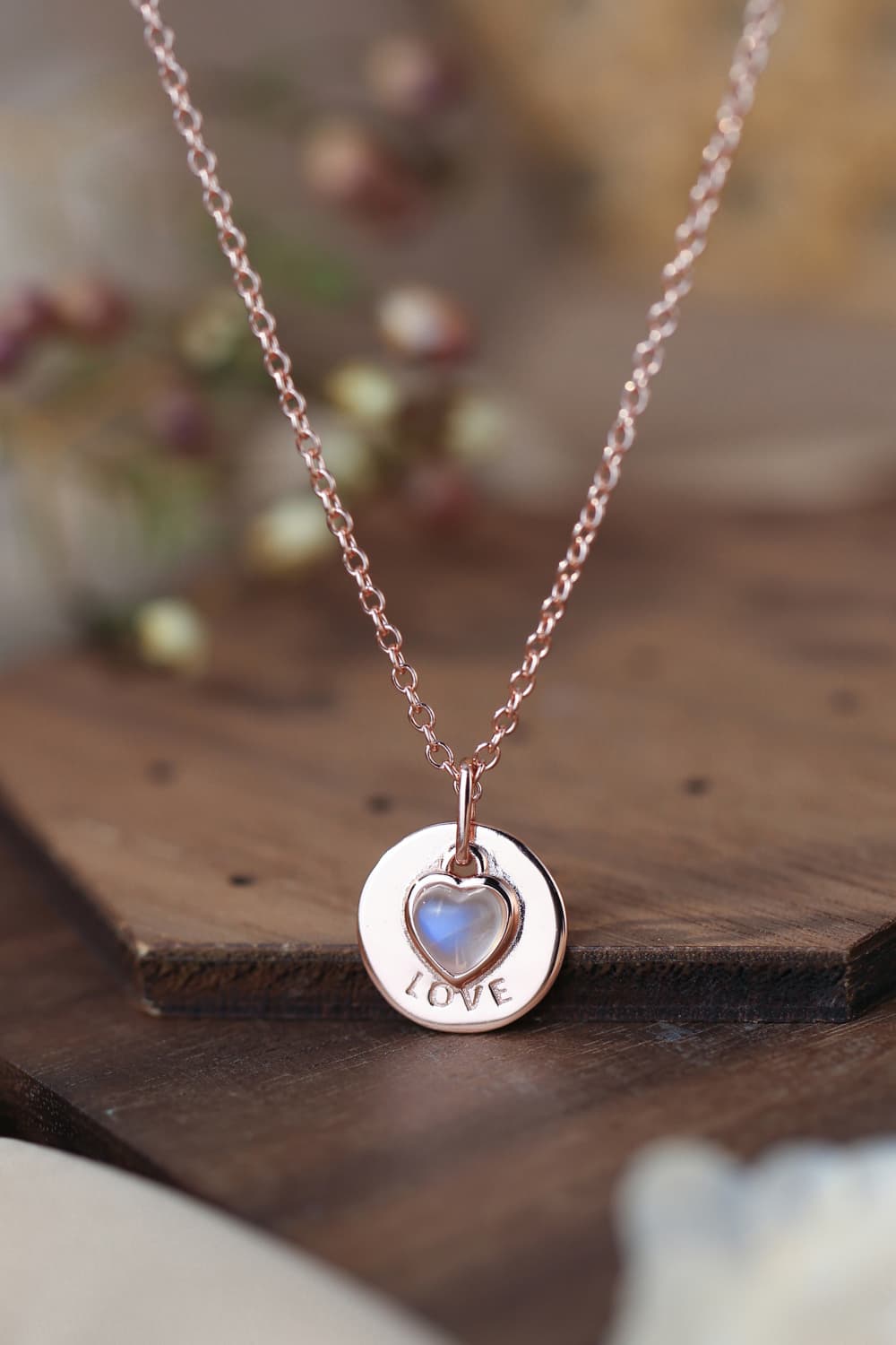 "Photograph of a Moonstone LOVE Heart Pendant hanging from a delicate 925 Sterling Silver Necklace. The heart-shaped pendant showcases a luminous moonstone with captivating blue and white hues, exuding an ethereal glow. The necklace's intricate silver chain complements the pendant's elegance. A perfect blend of nature's beauty and craftsmanship."